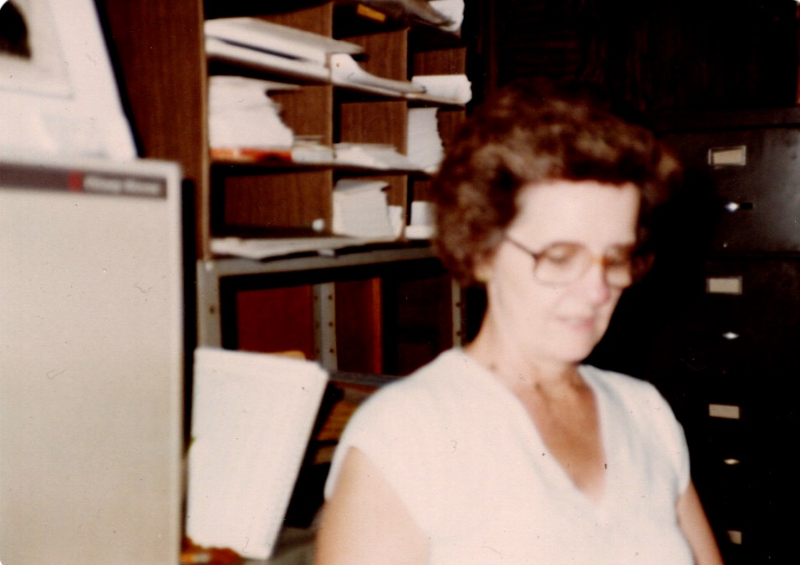 A vintage photograph of Ann Snipes working in her tax office surrounded by files